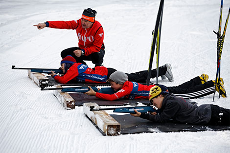 Ein Biathlon-Trainer gibt Anweisungen, während die Kinder liegend ihre Schüsse abgeben.