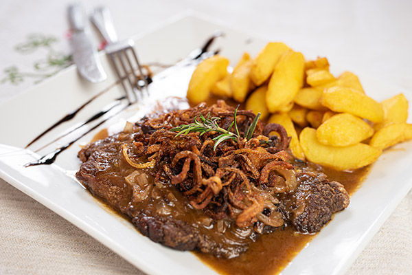 Ein Teller mit Zwiebelrotstbraten und Bratkartoffeln auf den Tisch gestellt.